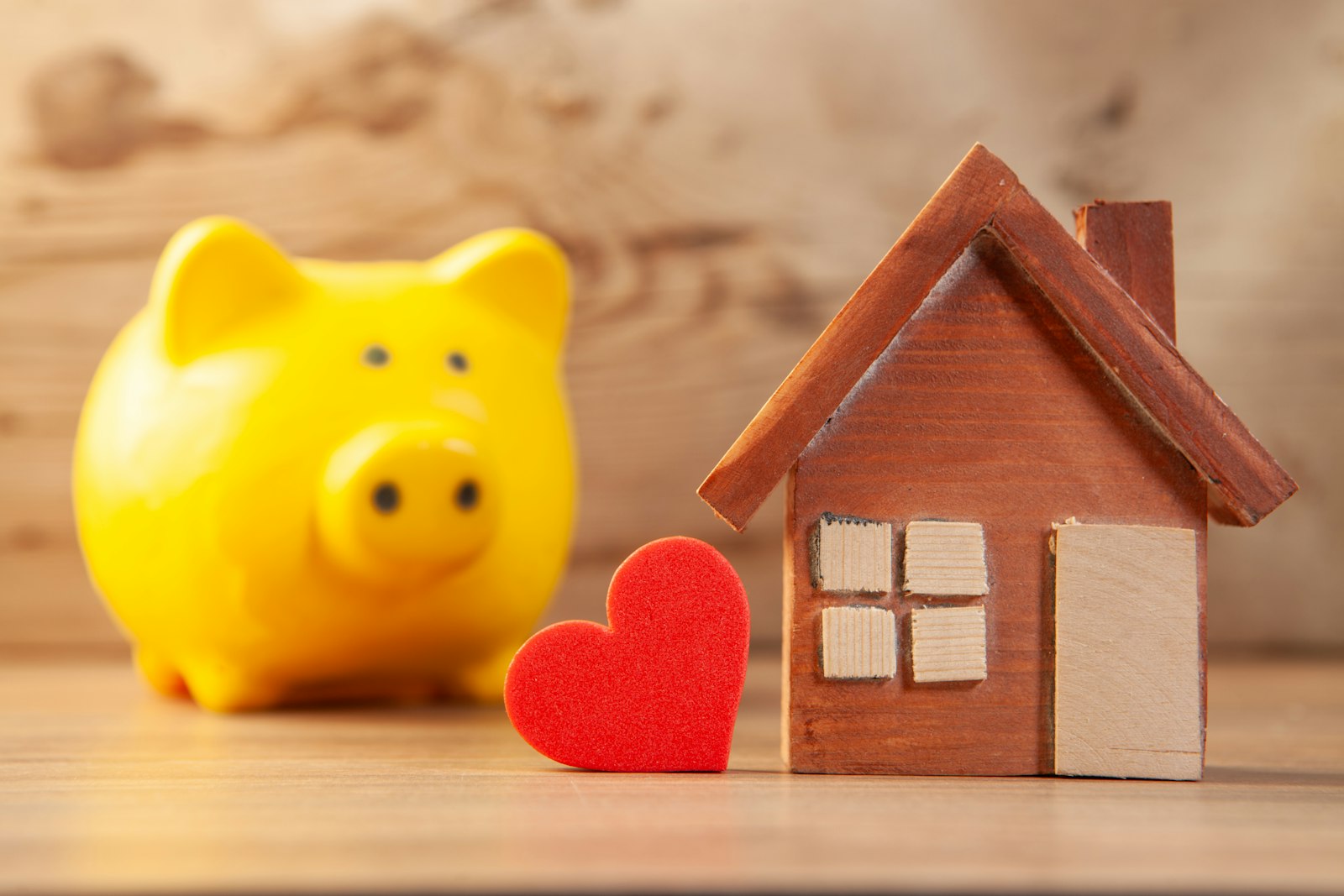 a yellow piggy bank beside a small wooden house model