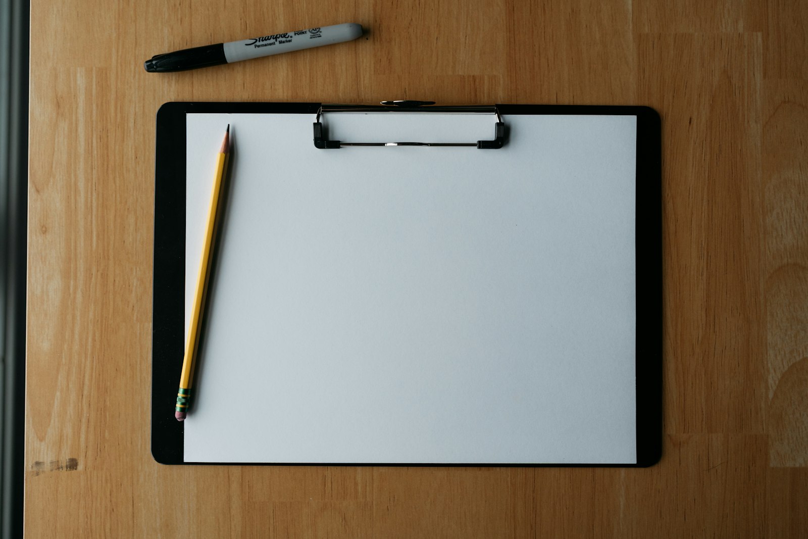 a clipboard, pencil, and pen on a wooden surface