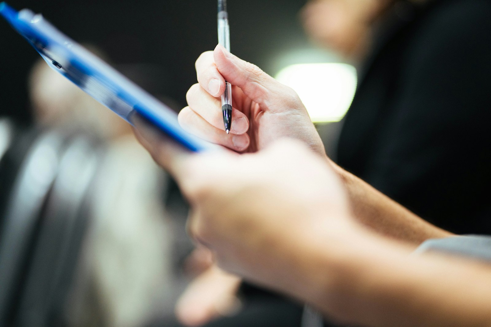 a hand holding a pen over a blue clipboard