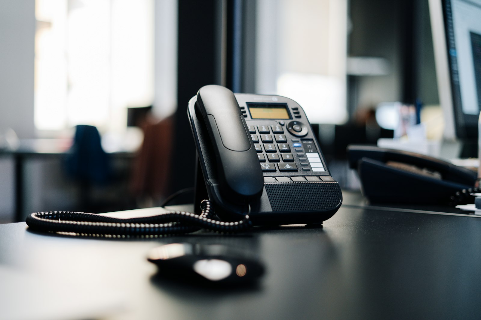 a black ip desk phone on a black wooden table